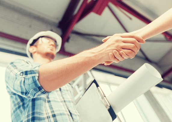 Contractor in a hard hat shaking hands over a set of building plans