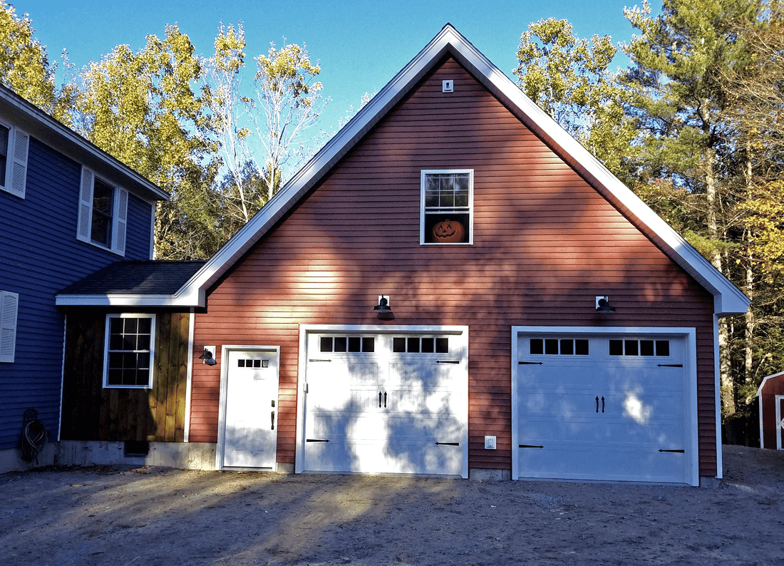 Barn red two car garage with a loft window and white carriage style doors, beside a blue house