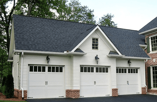 Three car attached garage with white siding, a brick base and lanterns between the doors