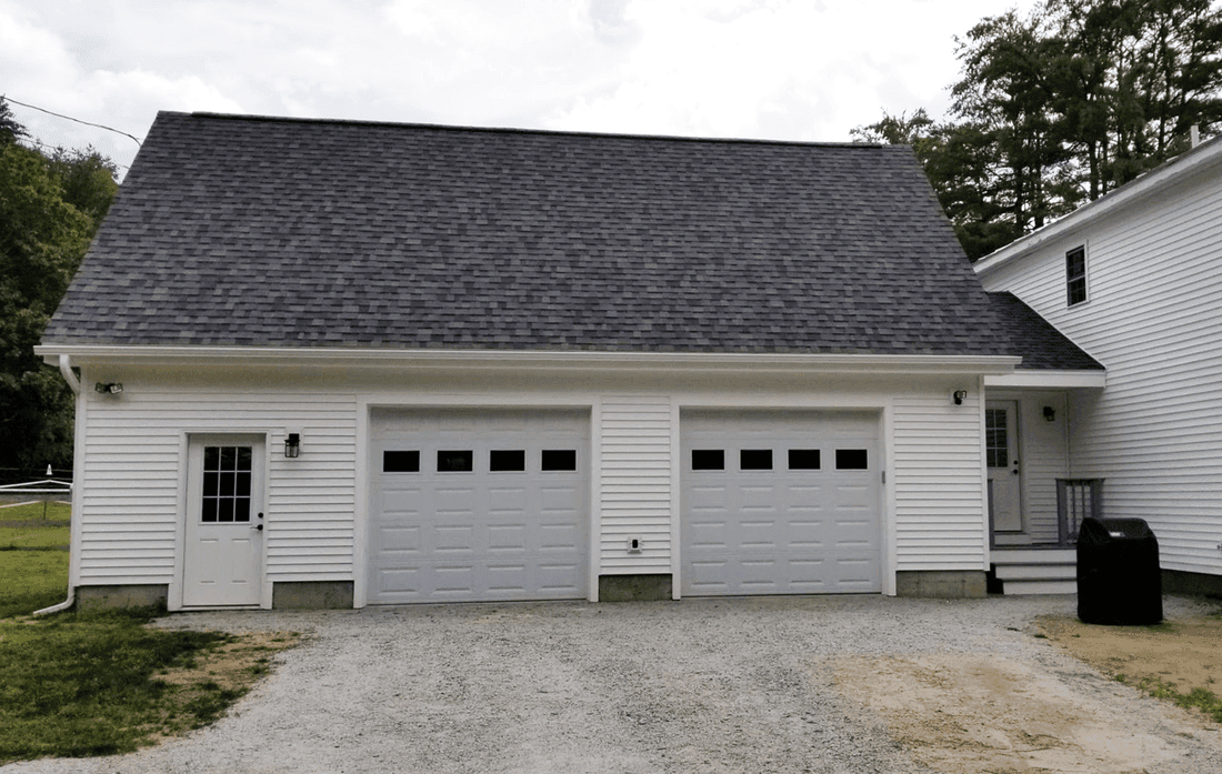 White two car garage with a long roofline, built beside the house at the end of a gravel driveway